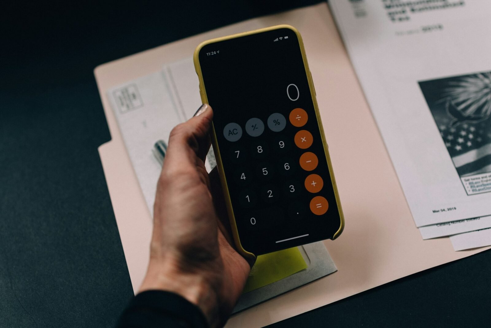 A hand holding a smartphone calculator over paper financial forms