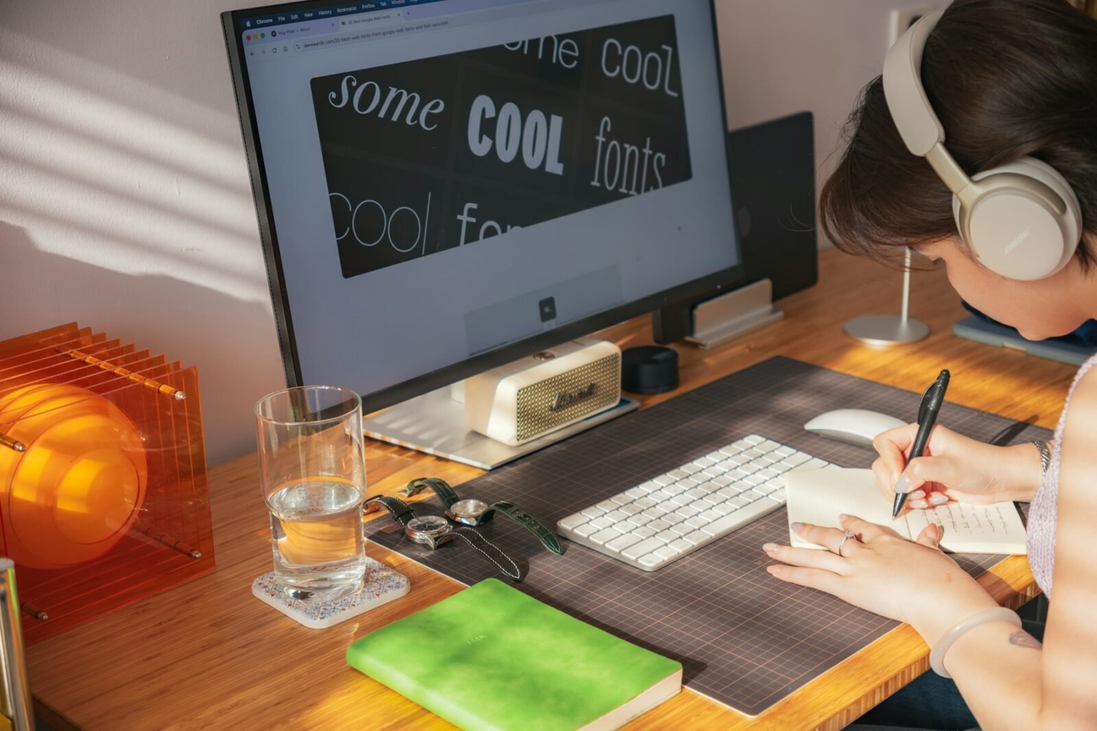 Person in headphones writing in a notebook at a sunlit wooden desk