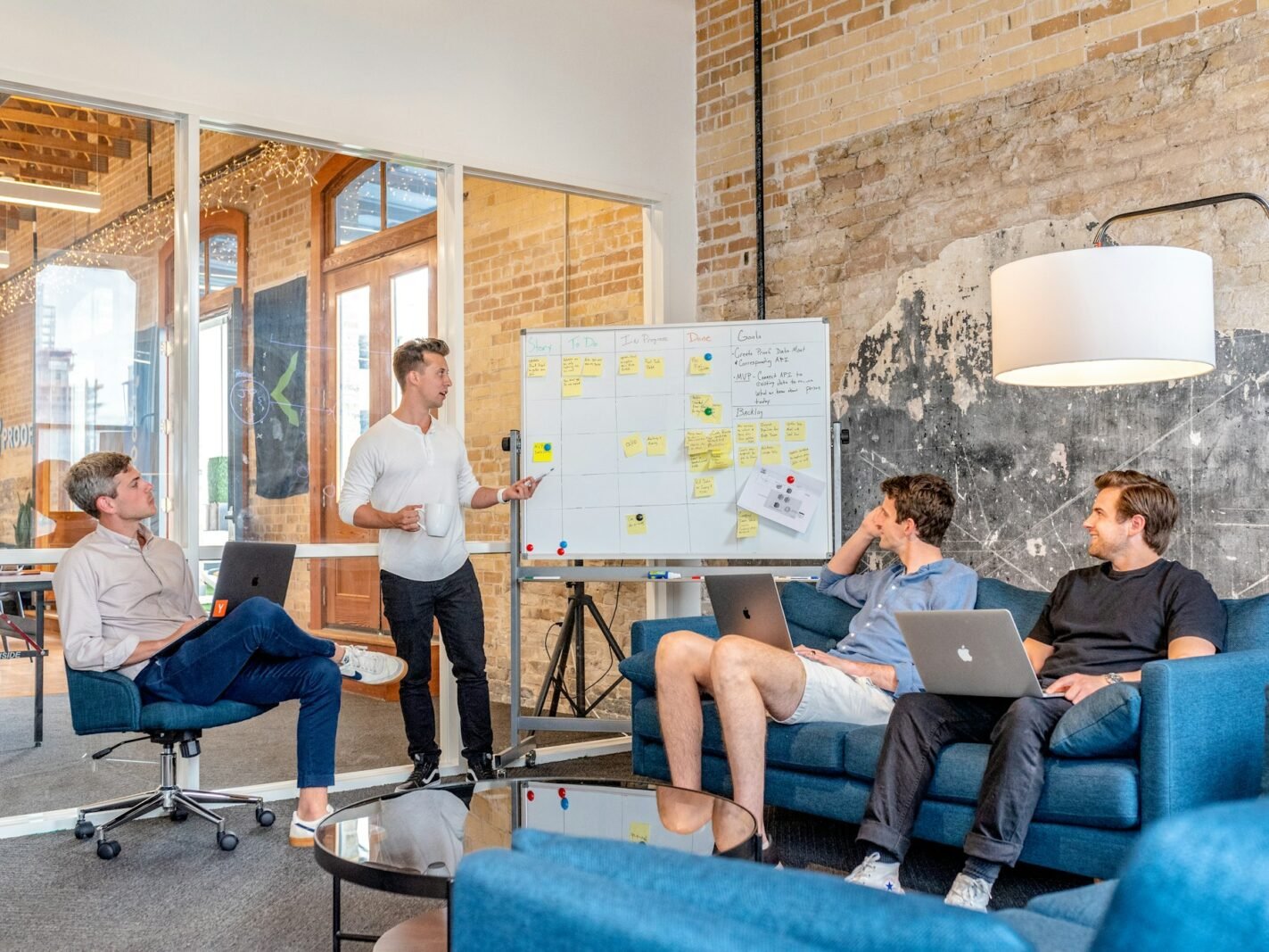A sales team with laptops watching a colleague present at a whiteboard